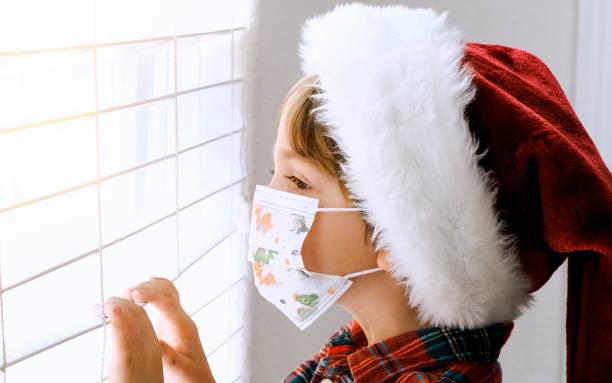 istock Little boy wearing a Santa hat and a protective face mask looking through a window waiting for Santa to came 1278694269