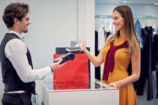istock Young woman is paying using mobile phone in a boutique 1278694927