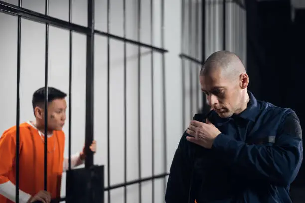 Photo of A stern, bald prison warden makes the rounds of the cells and transmits information over the radio to the head of the prison guard