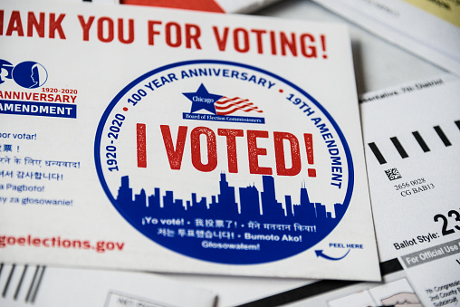 Close up of Sticker with I Voted! printed legend and other paper work.\nThe Voting-by-mail allows voters who cannot or do not want to visit the polls on Election Day, to cast their ballot by the US mail.