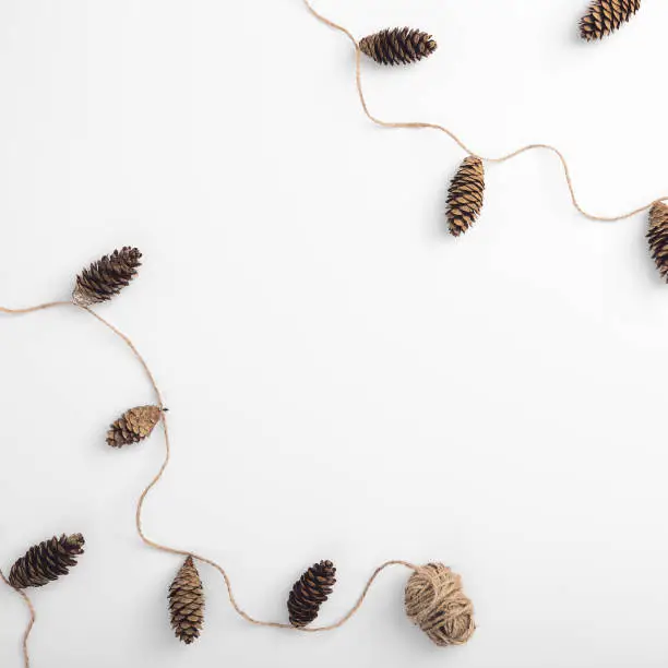Christmas minimal concept - Zero waste christmas garland made from pine cone and natural jute twine. Square composition, flat lay, top view. Eco friendly minimal christmas mockup with copy space.