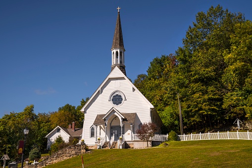 This image shows the front view of an old idyllic rural, small town church chapel building on top of a green hill.