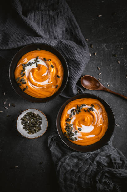 Vegetarian autumn pumpkin cream soup with seeds Vegetarian autumn pumpkin cream soup with seeds on dark background squash soup stock pictures, royalty-free photos & images