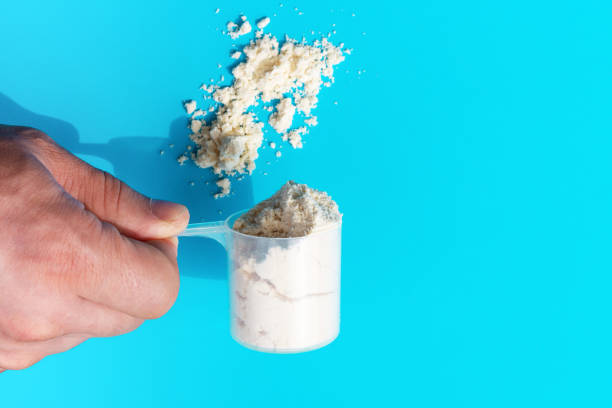 istock Male hand holds a measuring spoon with protein on blue background top view. 1278723502