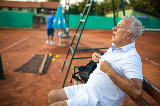 Senior man taking a break to catch some air on bench beside tennis court