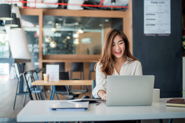 Happy young asian businesswoman sitting on her workplace in the office. Young woman working at laptop in the office. Happy young asian businesswoman sitting on her workplace in the office. Young woman working at laptop in the office. office laptop stock pictures, royalty-free photos & images