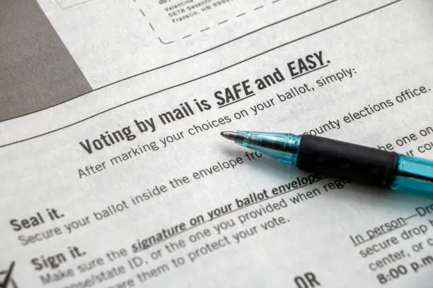 A booklet page of voter information, focused on the heading 'Voting by Mail is SAFE and EASY' with a pen laying on top.