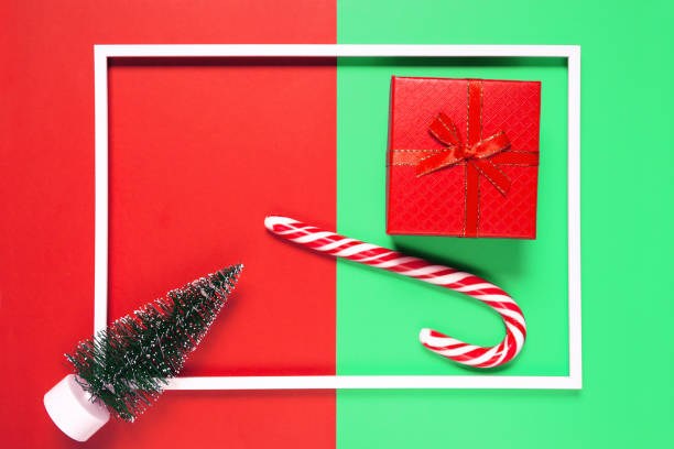 istock Chrismas composition with present box, decorative fir tree and lollipop on red and green background with white frame. Winter holiday concept. 1278729985