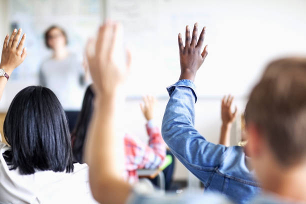 istock Teenage students raising hands in classroom 1278732337