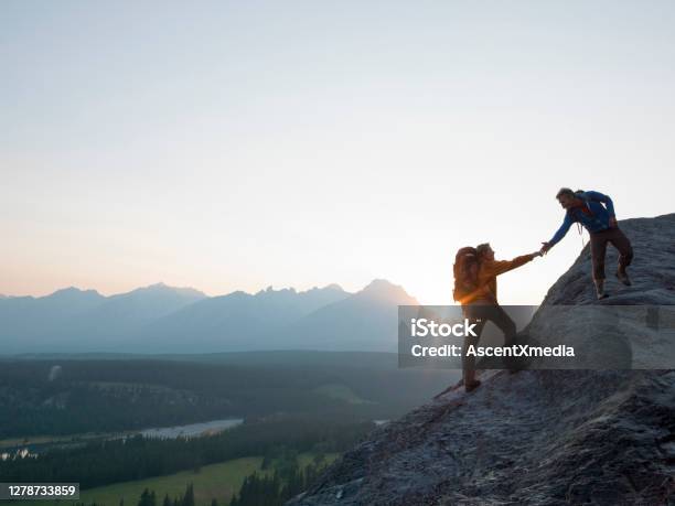 Two Mountaineers Offer Helping Hand On A Rock Ridge At Sunrise Above A Valley Stock Photo - Download Image Now