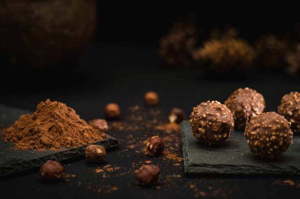 caramelos de chocolate espolvoreados con avellanas sobre un plato negro y cacao - anise baked biscuit brown fotografías e imágenes de stock