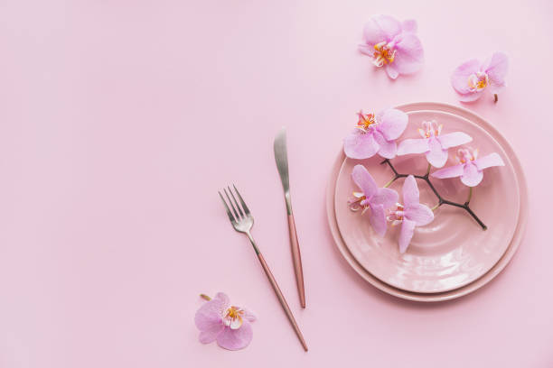 istock Flower and table settings overhead composition on light pink background. Pink ceramic plates, cutlery and perple orchid flowers. Holiday modern table decoration. Romantic date. 1278742874