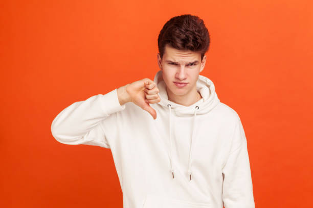 i don't like this. young man in casual style hoodie showing thumb down sign with disgust on his face, application testing feedback - rudeness ugliness clothing people imagens e fotografias de stock