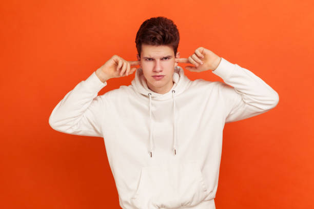 Don't want to hear! Angry teenager in stylish sweatshirt with hood closing ears with fingers, disobedience, ignoring annoying noise Don't want to hear! Angry teenager in stylish sweatshirt with hood closing ears with fingers, disobedience, ignoring annoying noise. Indoor studio shot isolated on orange background man closing ears photos stock pictures, royalty-free photos & images
