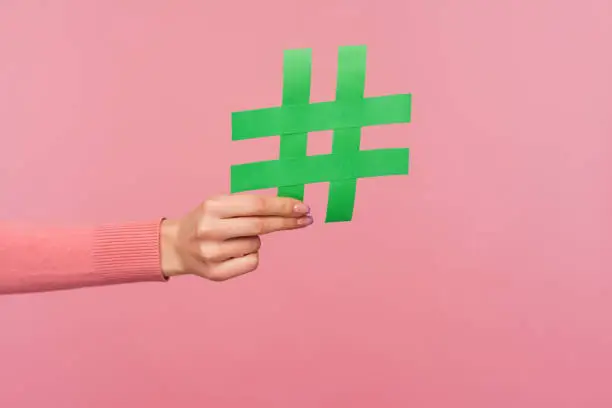 Photo of Join popular blog! Closeup of female hand holding green hashtag sign, sharing tagged message, recommending follow trends