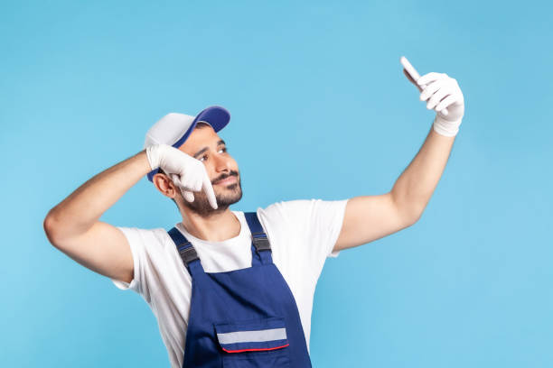 istock Worker in overalls and gloves pointing finger down while talking on video call, communicating online 1278743951