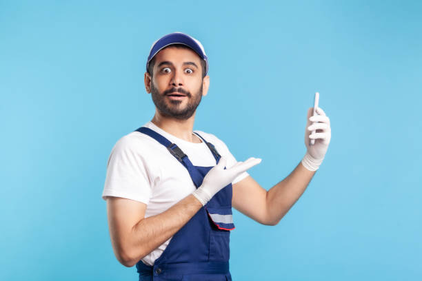 istock Surprised workman in overalls pointing mobile phone and looking amazed, shocked by online purchase order app 1278743955