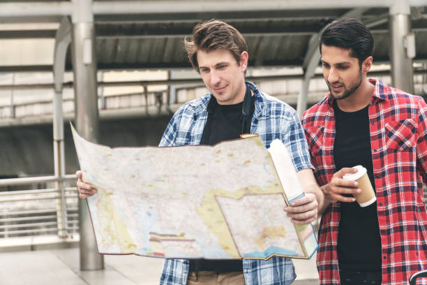 istock Two traveler handsome guys searching for direction using map paper while standing in city. Tourist young man looking map on vacation for some destinations with her friend. Travel lifestyle concept. 1278744383