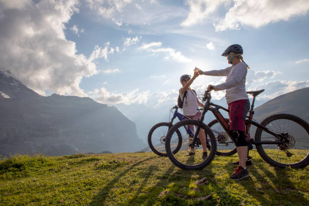 e-bikers de montagne féminins haut cinq dans le pré alpin - berne alps photos et images de collection