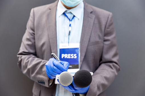 Reporter at press conference or media event wearing protective gloves and face mask against coronavirus COVID-19 disease