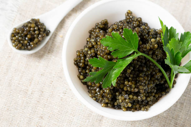 istock Black caviar. Black sturgeon caviar in a ceramic bowl and in a ceramic spoon on a light background. Useful delicacy. Top view with space for text 1278754799