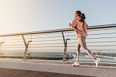 Healthy young girl running on the sea side promenade. Female runner working out on a sunny morning.