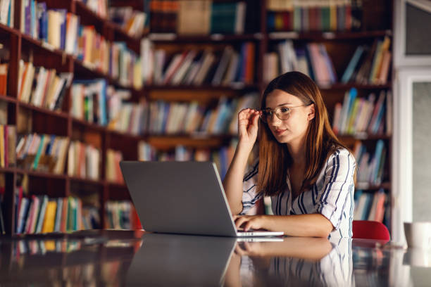도서관에 앉아 노트북을 사용하여 젊은 미소 매력적인 대학생. 그녀는 숙제를 쓰고 있습니다. - professor librarian university library 뉴스 사진 이미지