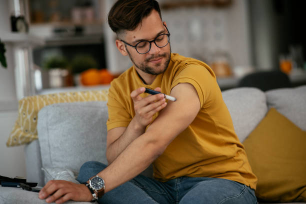 Young man giving himself an insulin shot at home. stock photo