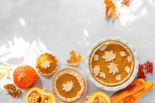 Sunny autumn day pumpkin pie baking at home background, fall traditional food recipes, top down view of baked pie and autumn leaves, copy space for a text