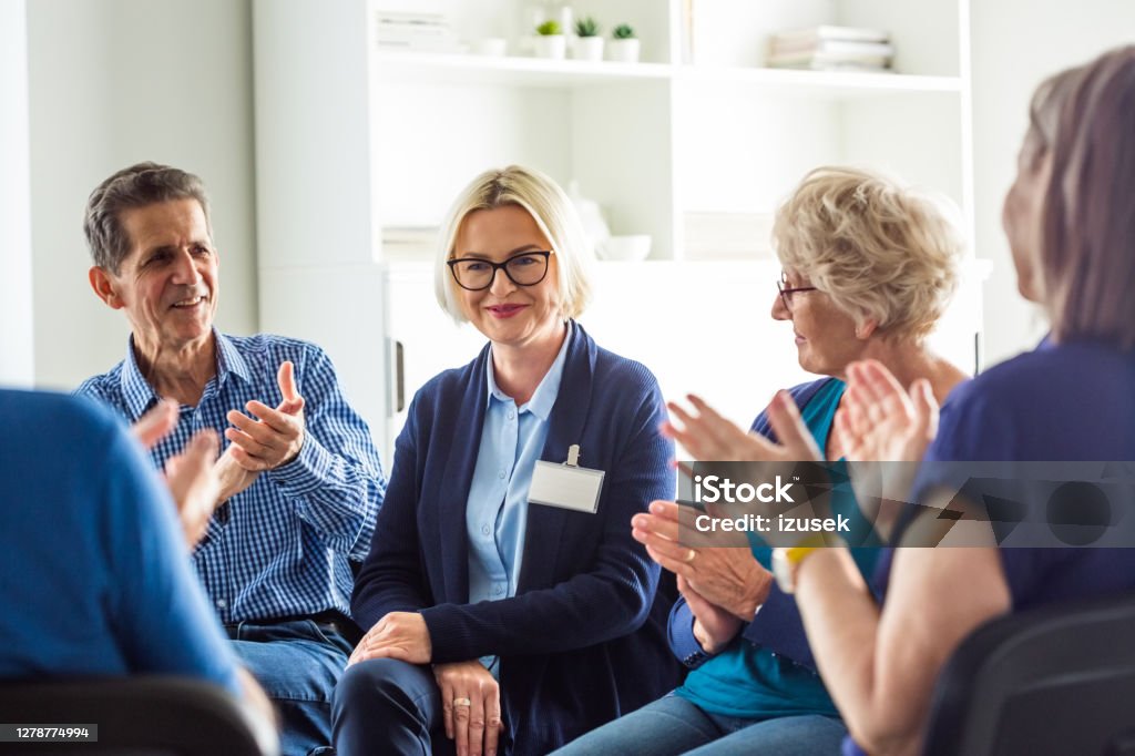 Psychotherapist talking with senior people Senior people sharing issues with patients and coach during meeting in nursing home. Mental health professional is sitting with people at community center. They are discussing about mental wellbeing. 70-79 Years Stock Photo