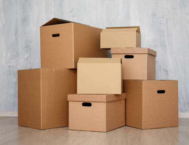 istock moving day or postal delivery concept - brown cardboard boxes stacked on the floor over gray wall 1278774997