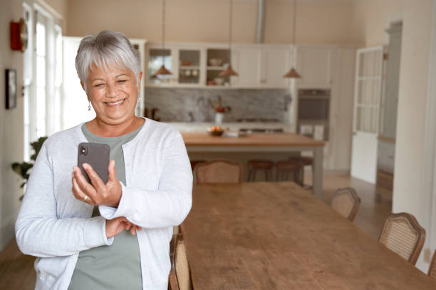 Happy elderly woman using cellphone Happy elderly woman using cellphone at home in her kitchen convenience photos stock pictures, royalty-free photos & images