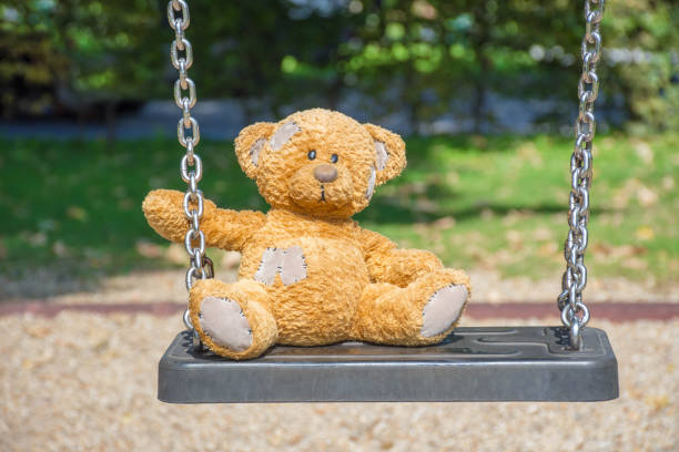 istock Cute little teddy bear standing alone on a swing in empty park on a beautiful sunny day. 1278777541
