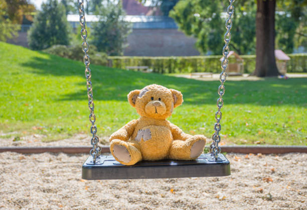 istock Cute little teddy bear standing alone on a swing in empty park on a beautiful sunny day. 1278777569