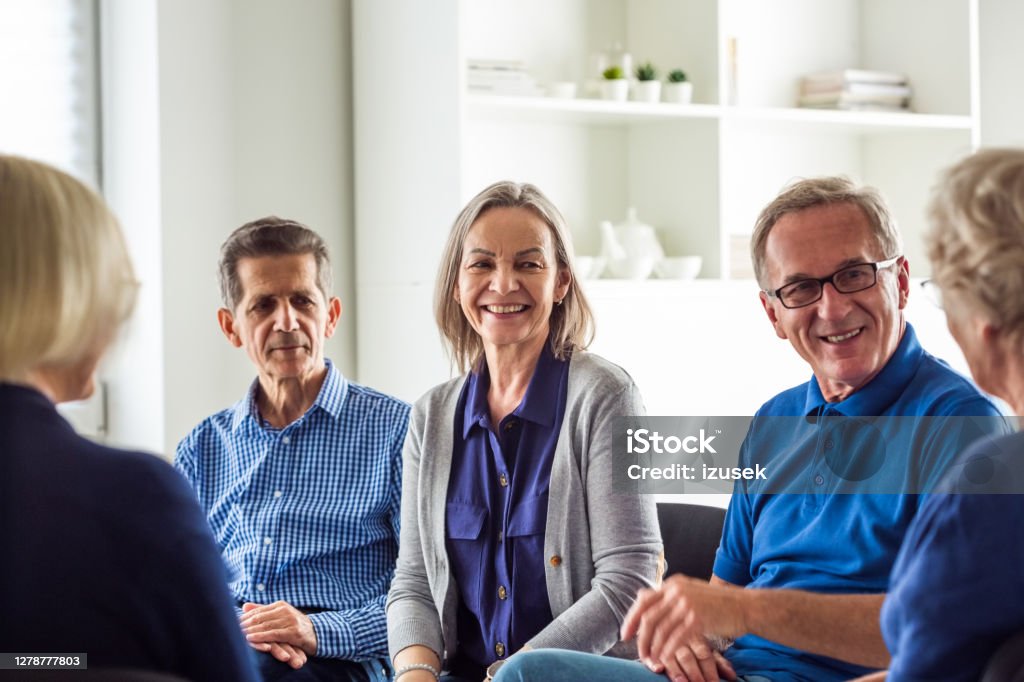 Senior people during group therapy Senior people sharing issues with patients and coach during meeting in nursing home. Mental health professional is sitting with people at community center. They are discussing about mental wellbeing. Meeting Stock Photo