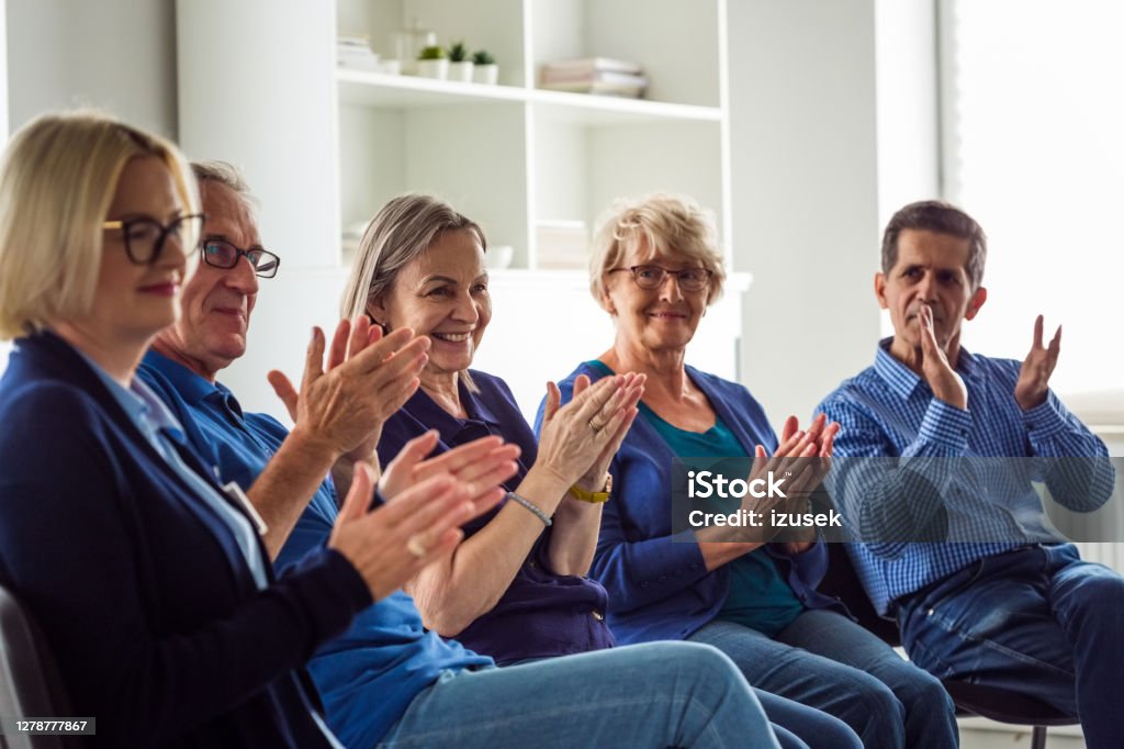 Senior people during group therapy Senior people sharing issues with patients and coach during meeting in nursing home. Mental health professional is sitting with people at community center. They are discussing about mental wellbeing, clapping hands. 70-79 Years Stock Photo