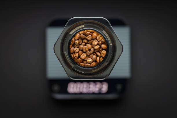 Aeropress coffee maker with scales on a black background top view. Aeropress with coffee beans in focus, background blurred.