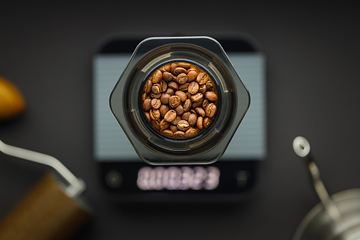 Aeropress coffee maker with scales, coffee grinder and kettle on a black background top view. Aeropress with coffee beans in focus, background blurred.