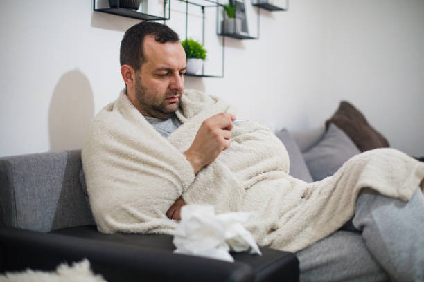 istock Sick man in bed checking fever with thermometer 1278780677