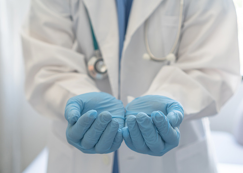 Medical doctor or surgeon with empty hands in hygience lab gloves offering or holding copy space for health care practice, nursing, organ donation, hospital csr, or clinical charity concept