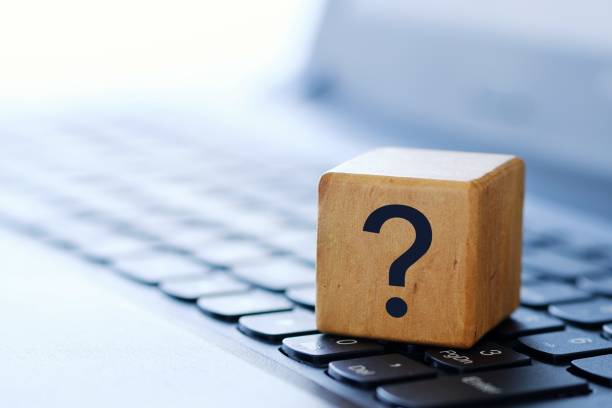 A question mark on a wooden cube on a computer keyboard, with a blurred background and shallow depth of field. stock photo