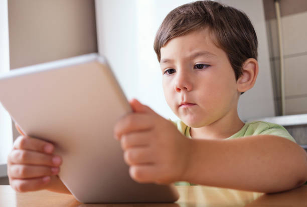 istock Cute boy sitting at the table and watching video on the tablet 1278785968