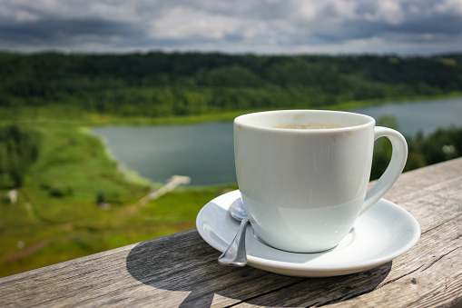 White cup of hot coffee on balcony with natural and mountains, hills background. Copy space. Beverage, breakfast.