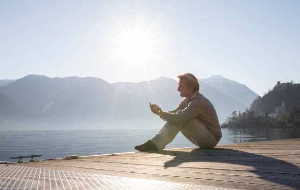 istock Man uses mobile phone on a pier over a lake at sunrise 1278787702