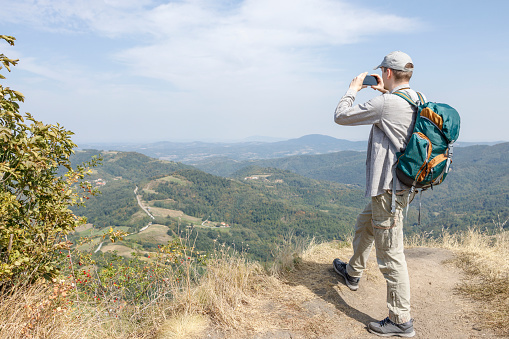 Man taking photos with smart phone during hiking rest on the hill