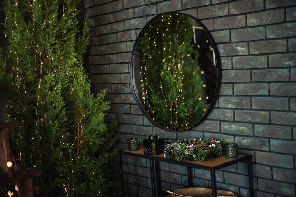 istock On a khaki brick green wall hangs a round mirror with a black frame. Around the Christmas trees in garlands with lights, juniper. Wallpaper for advertising, text, blurred background. Copy space place 1278794310