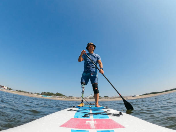 amputierter mann paddelboarding im meer - amputiert stock-fotos und bilder