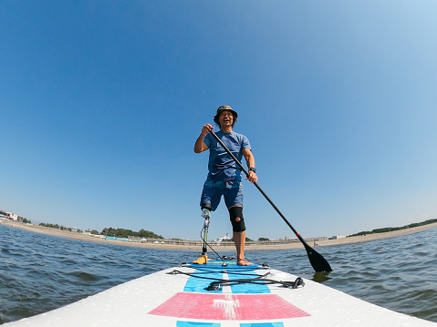 A font view of an amputee man paddle boarding in the sea.
