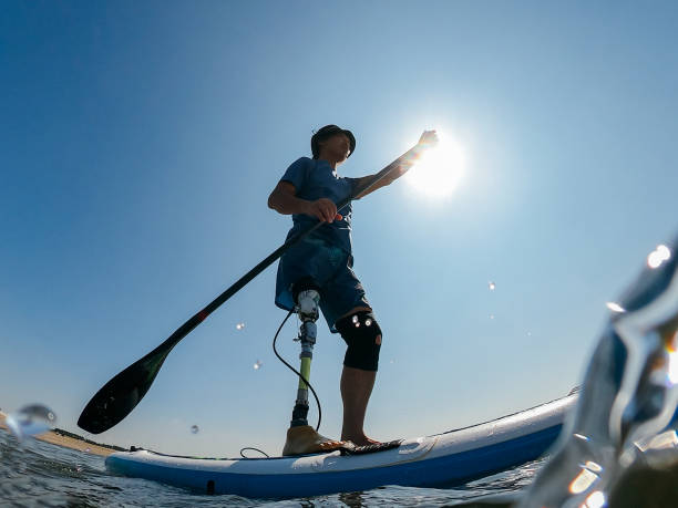 Amputee man paddle boarding in sea A font view of an amputee man paddle boarding in the sea. paddleboard surfing water sport low angle view stock pictures, royalty-free photos & images