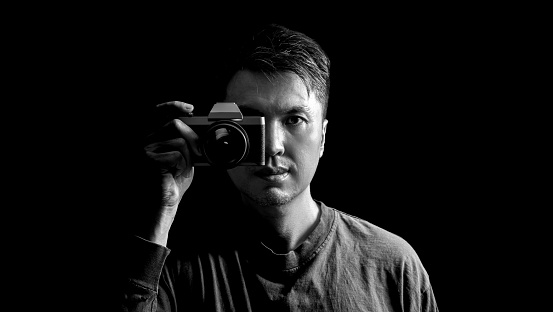black and white asian man holding retro camera, isolated on black